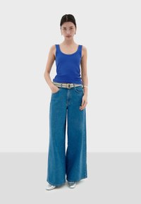 Blauw geribbelde tanktop gecombineerd met wijde blauwe spijkerbroek. Opvallende zilveren riem, oversized pasvorm en glanzend zilveren schoeisel. Eenvoudig ontwerp.