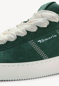 Sneaker verde in suede con spesse lacci bianchi intrecciati, suola bianca testurizzata e dettagli in bianco a contrasto sulla cucitura e sul logo.