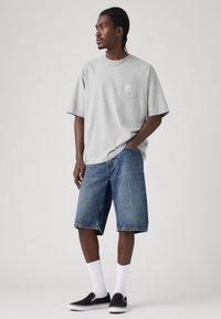 Gray short-sleeve T-shirt with pocket, blue denim shorts, white socks, and black slip-on shoes. Simple design, casual fit.
