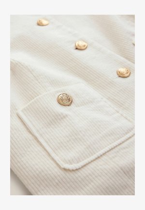 White corduroy fabric with a ribbed texture, featuring gold buttons and a flap pocket with a decorative button detail.