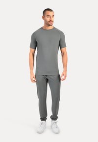 Grijze sportoutfit met een aansluitend kortmouwtop en taps toelopende broek met elastische manchetten, gemaakt van een gladde, rekbare stof. Witte sneakers.