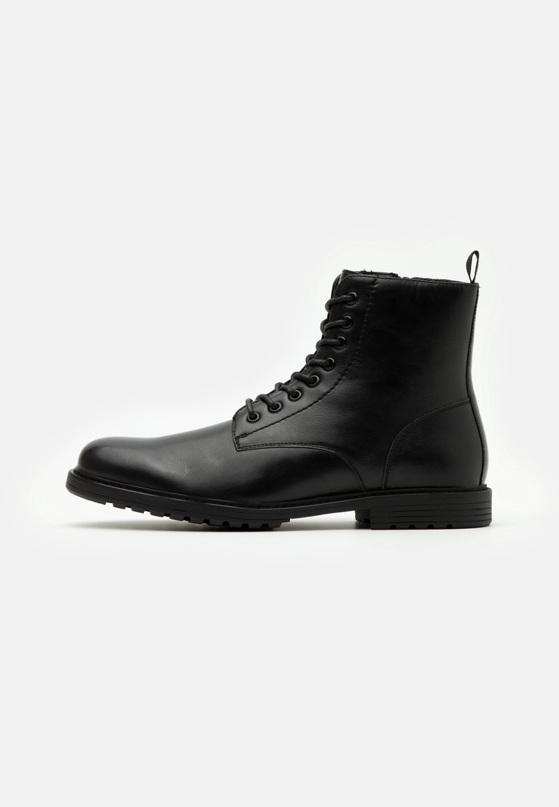 Bottine en cuir noir à lacets avec semelle épaisse et languette au talon, vue de profil sur fond blanc.