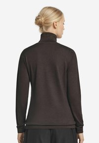 Brun långärmad topp med hög krage, tillverkad av ett mjukt material. Har en slät yta och en åtsittande design som sträcker sig ner till höfterna.