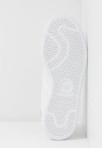 Semelle de basket blanche présentant une texture en alvéoles, un design incurvé et un logo en relief. Le matériau semble être du caoutchouc avec une finition lisse.
