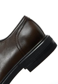 Zapato de cuero marrón con un acabado suave, punta redondeada, costuras en contraste y una suela de goma negra con acentos texturizados.