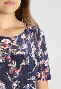 Marinebluse aus Spitze mit floralen Mustern in Pink und Weiß, kurzärmlig und mit rundem Ausschnitt, zeigt eine leichte, transparente Textur.
