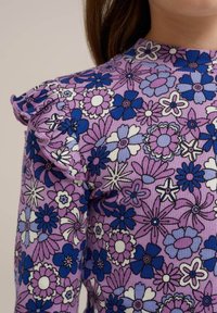 Top cu model floral în nuanțe de violet, cu detalii volan la umeri, prezentând flori albastre, albe și roz pe un material texturat.