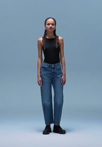 Zwarte mouwloze bodysuit, hoge taille lichtblauwe spijkerbroek, rechte snit, middelmatige wassing en zwarte veterschoenen.