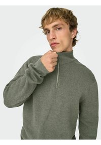 Szary sweter z zamkiem błyskawicznym przy szyi, o fakturze prążkowanej, z długimi rękawami i stójką. Posiada metalowy zamek oraz dopasowane mankiety.