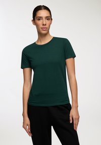 Zielona koszulka z krótkim rękawem, uszyta z miękkiego materiału, z okrągłym dekoltem, zestawiona z czarnymi spodniami, charakteryzująca się wygodnym i swobodnym stylem.