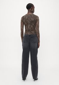 Long-sleeve fitted top in brown and black animal print, paired with high-waisted, loose-fitting dark gray jeans and black heeled shoes.