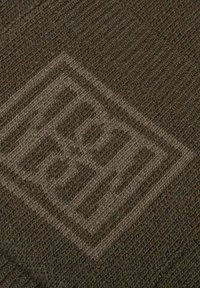 Donkerbruin gebreide stof met een textuurpatroon. Bevat een reliëflogo-detail. De oppervlakte lijkt zacht en iets rekbaar.