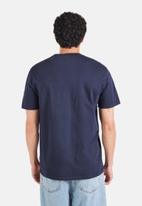 Camiseta de algodón azul marino con cuello redondo y mangas cortas. La vista trasera revela una textura suave y un diseño simple sin logotipos visibles.