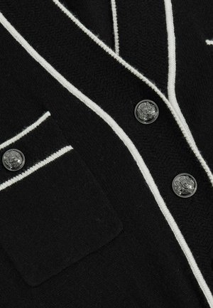 Černý cardigan s bílé pruhovanými detaily, texturovanou tkaninou, dvěma stříbrnými knoflíky a náprstkovou kapsou na levé straně.