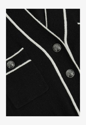 Černý cardigan s bílé pruhovanými detaily, texturovanou tkaninou, dvěma stříbrnými knoflíky a náprstkovou kapsou na levé straně.