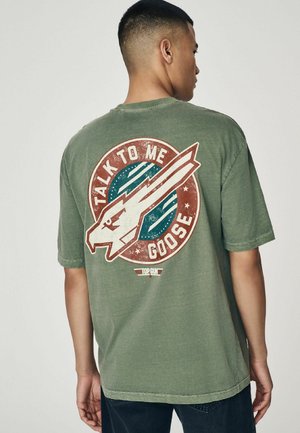 Olivengrøn bomulds T-shirt med en stor rund grafik på ryggen, der viser en stiliseret fugl, teksten "TALK TO ME GOOSE" og slidte teksturer.