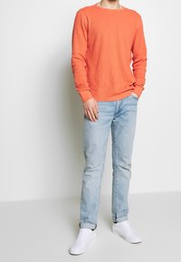 T-shirt orange à manches longues côtelé associé à un jean bleu clair et des baskets blanches. Le t-shirt présente un col rond et des manches ajustées.