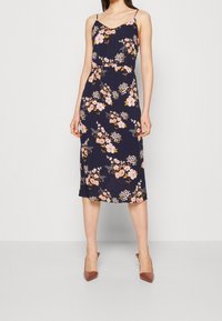 Blommig midi klänning med justerbara spaghettiband. Marinblå bakgrund med rosa och vita blommor. Lättviktsmaterial, figurnära midja och samlad detalj.