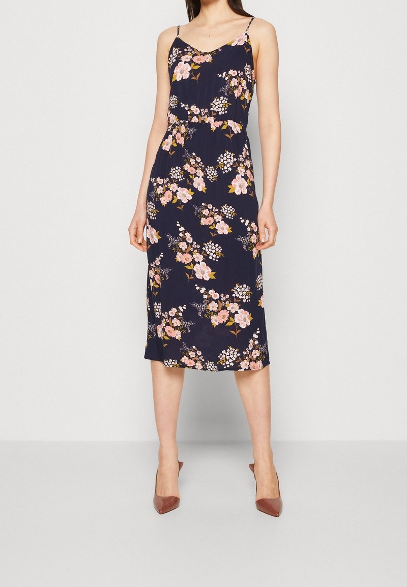 Blommig midi klänning med justerbara spaghettiband. Marinblå bakgrund med rosa och vita blommor. Lättviktsmaterial, figurnära midja och samlad detalj.
