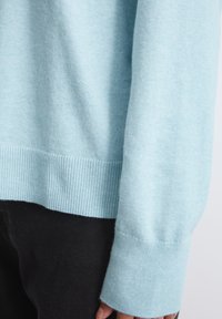 Vaaleansininen neulepaita, joka on valmistettu pehmeästä neulemateriaalista. Siinä on ribbireunat ja hihansuut. Tekstuurin pinta näyttää sileältä ja hieman pörröiseltä.