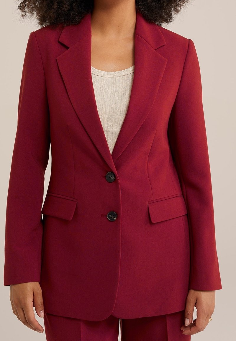 Bordowy żakiet wykonany z sformalizowanej tkaniny, z wyciętymi klapami, dwiema przednimi kieszeniami i dwoma czarnymi guzikami z przodu.