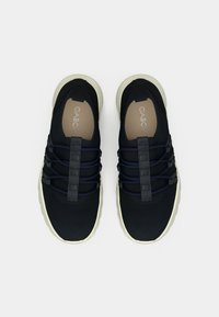 Ζευγάρι μαύρα sneakers χωρίς κορδόνια με λευκές σόλες και ελαστικά κορδόνια, με την επωνυμία "Gabor" εμφανή στις ταμπανιασμένες εσωτερικές σόλες, σε θέα από πάνω.