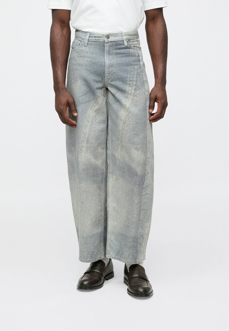 Lyseblå vide jeans med falmet, teksturert finish, høy midje, fem lommer og glidelås, kombinert med mørke sko.