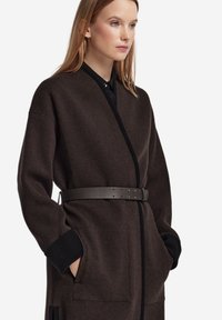 Brauner Mantel aus Wollmischung mit Wickeldesign, kontrastierenden schwarzen Akzenten, großen Taschen und breitem Lederbund in der Taille.