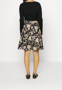 Svart långärmad topp med fyrkantig ringning, tillsammans med en knälång utsvängd kjol med ett blommönster i kräm och rosa på en svart bakgrund.