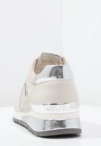 Michael Kors sneaker textúrált világosbézs felsőrésszel, ezüst részletekkel és fényes fém sarkal. Jellemzői között szerepel a strapabíró talp és a logó részlet.