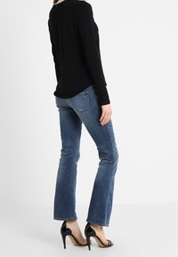 Top nero a maniche lunghe, jeans blu slim-fit, sandali neri con tacco alto. Il materiale sembra morbido, i jeans hanno un lavaggio sbiadito e una leggera zampa.
