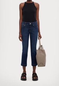 Žena v tmavě modrých zkrácených džínách, černém topu bez rukávů, černých platformových sandálech a s šedou taškou přes rameno.