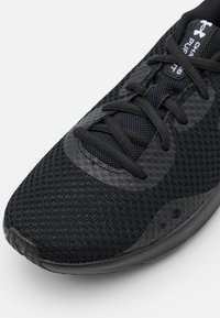 Scarpa sportiva nera con tomaia in rete testurizzata, punta rotonda e lacci piatti. Accenti lisci e branding notevole sulla linguetta.
