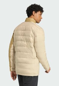 Padded jacket in beige with a contrasting brown shoulder, featuring horizontal quilted design and a high collar. Smooth, shiny texture.