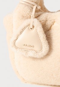 Kremfarget håndveske laget av plysj, teksturert materiale med en trekantet lærdetalj som har preget "ALDO". Jevn og myk overflate.