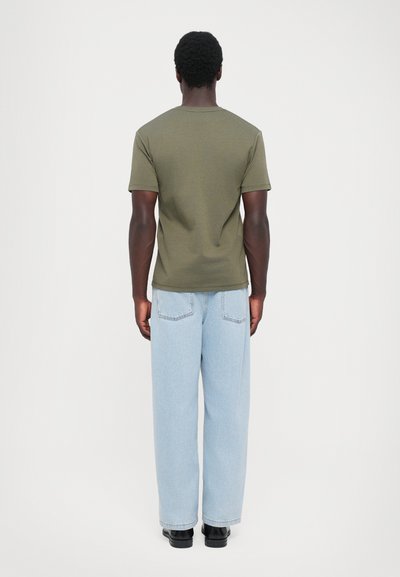 Olivengrønt kortærmet skjorte med rund hals, parret med lyseblå løse jeans og sorte sko. Bagfra.