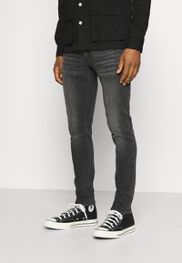 Jeans oscuros de corte ajustado combinados con zapatillas altas negras con acentos blancos. El conjunto incluye una camisa negra de botones.