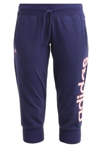 Tummansinisiä lyhennettyjä collegehousuja, jotka on valmistettu pehmeästä materiaalista. Housuissa on sivutaskut, joustava vyötärö ja vaaleanpunainen "adidas"-logo vasemmassa sääressä.