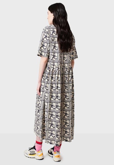 Abito midi stampato in beige e blu navy con un motivo geometrico, maniche corte, vita arricciata e gonna fluida. Indossato con sneakers e calze.