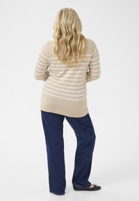 Knit beige sweater with white stripes, long sleeves, and a rounded hem; paired with loose dark blue jeans and black flat shoes.