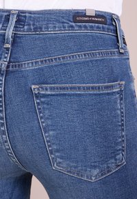 Vaqueros de mezclilla azules con un corte clásico, dos bolsillos traseros y un detalle de costura sutil. La etiqueta dice "CITIZENS of HUMANITY."