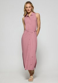 Abito rosa senza maniche, con bottoni frontali, colletto e cintura legata in vita. Lunghezza midi, tessuto liscio con spacchi laterali per facilitare i movimenti.