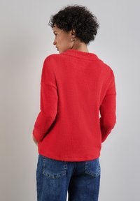 Maglione in pile rosso, testurizzato, con maniche a tre quarti e una finitura morbida, abbinato a pantaloni in denim blu. Design a scollo a V e vestibilità rilassata.