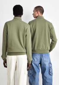 Olijfgroene sweaters met hoge kragen, gecombineerd met lichtgekleurde en blauwe cargobroeken. Eenvoudig ontwerp en zachte stoftextuur.