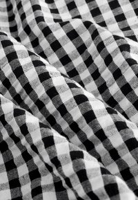 Schwarz-weiß kariertes Stoffmuster mit einem Rasterdesign. Die Quadrate sind gleichmäßig groß, mit einer weichen, strukturierten Oberfläche. Der Stoff fällt sanft.