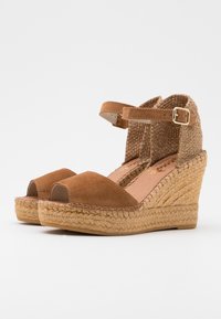 Sandalias de cuña de esparto de ante marrón con punta abierta, tira en el tobillo y detalle texturizado tejido en el talón. Suela intermedia de yute.
