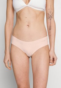 Ljust rosa sömlösa bikiniunderdelar med en slät yta och ett brett elastiskt midjeband. Har logotypdetalj på vänster sida.