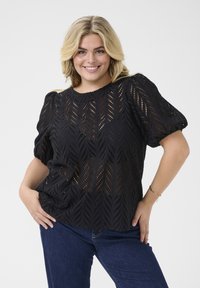 Black eyelet blouse with puff sleeves, featuring a chevron pattern and a round neckline. Material appears lightweight and textured.