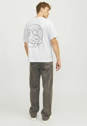 Hvid bomulds t-shirt med en sort stregtegning af et kranium på ryggen, parret med grå, let baggy denimjeans og hvide sneakers.