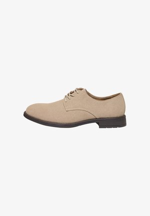 Chaussure habillée en daim beige pour homme avec lacets, semelle noire et petit talon, vue de profil sur fond blanc.